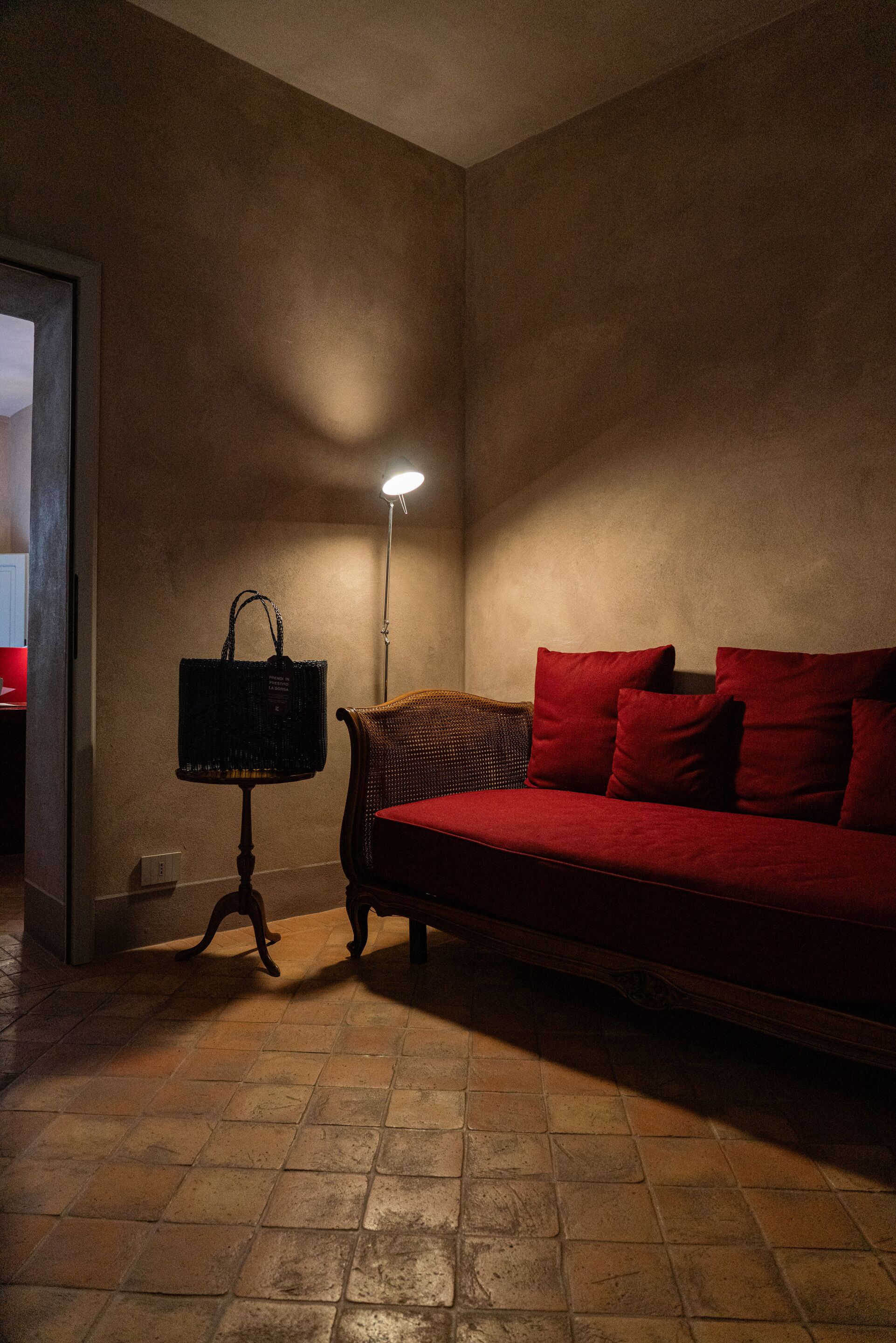 A dimly lit room with a red sofa, a wicker chair, and a floor lamp.