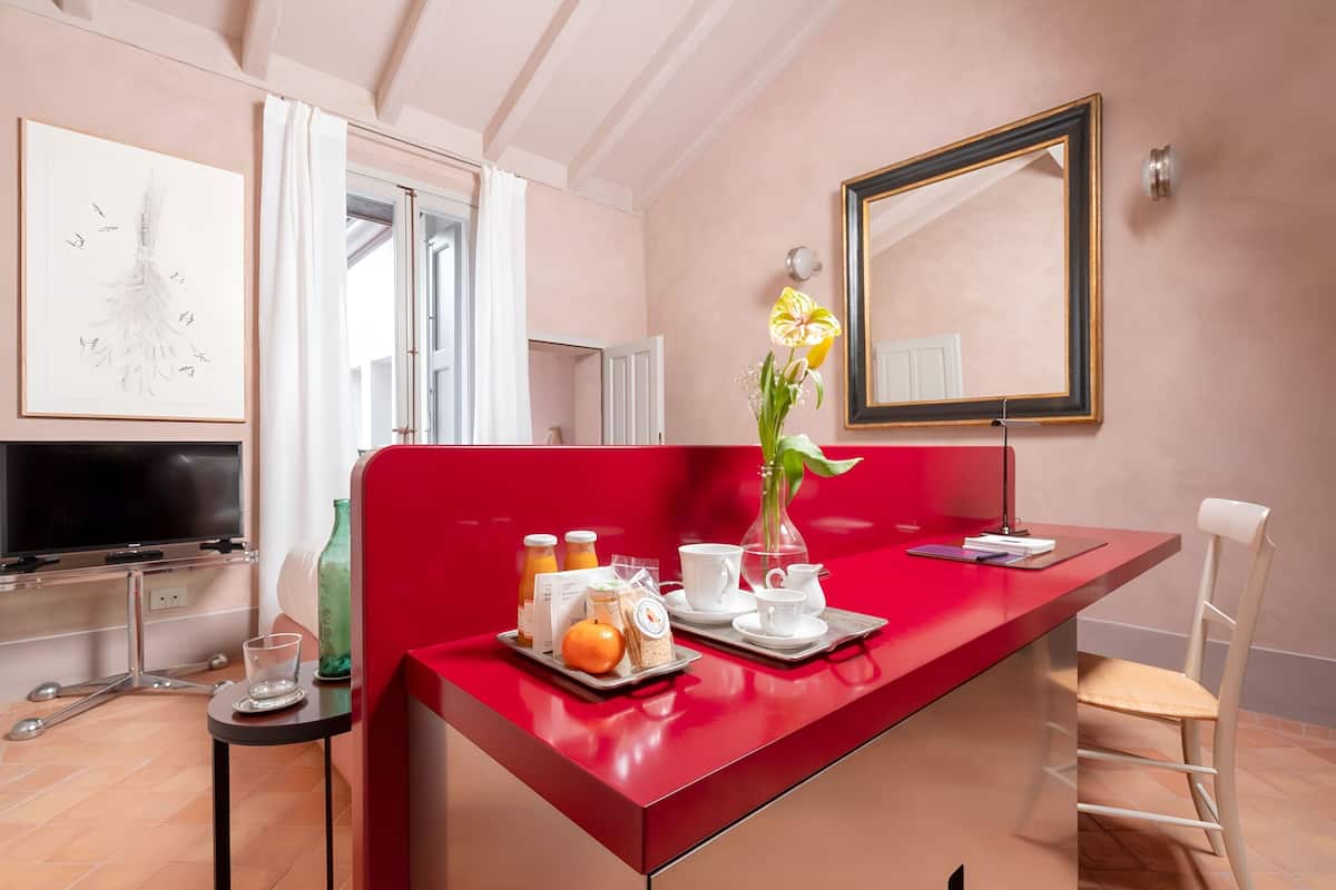 A modern room with a red accent wall, a dining table set with breakfast items, a large mirror, and a TV on the left.