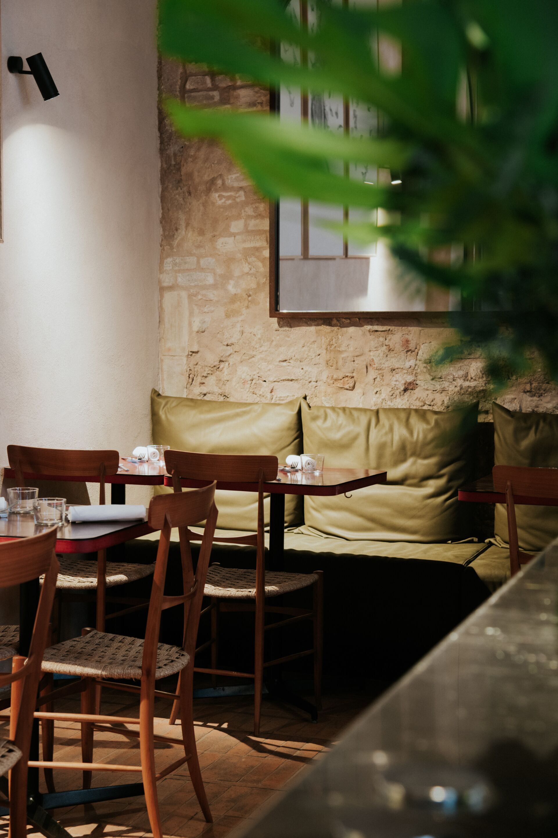 Un café acogedor con sillas y mesas de madera, una pared de piedra y un banco verde con cojín.