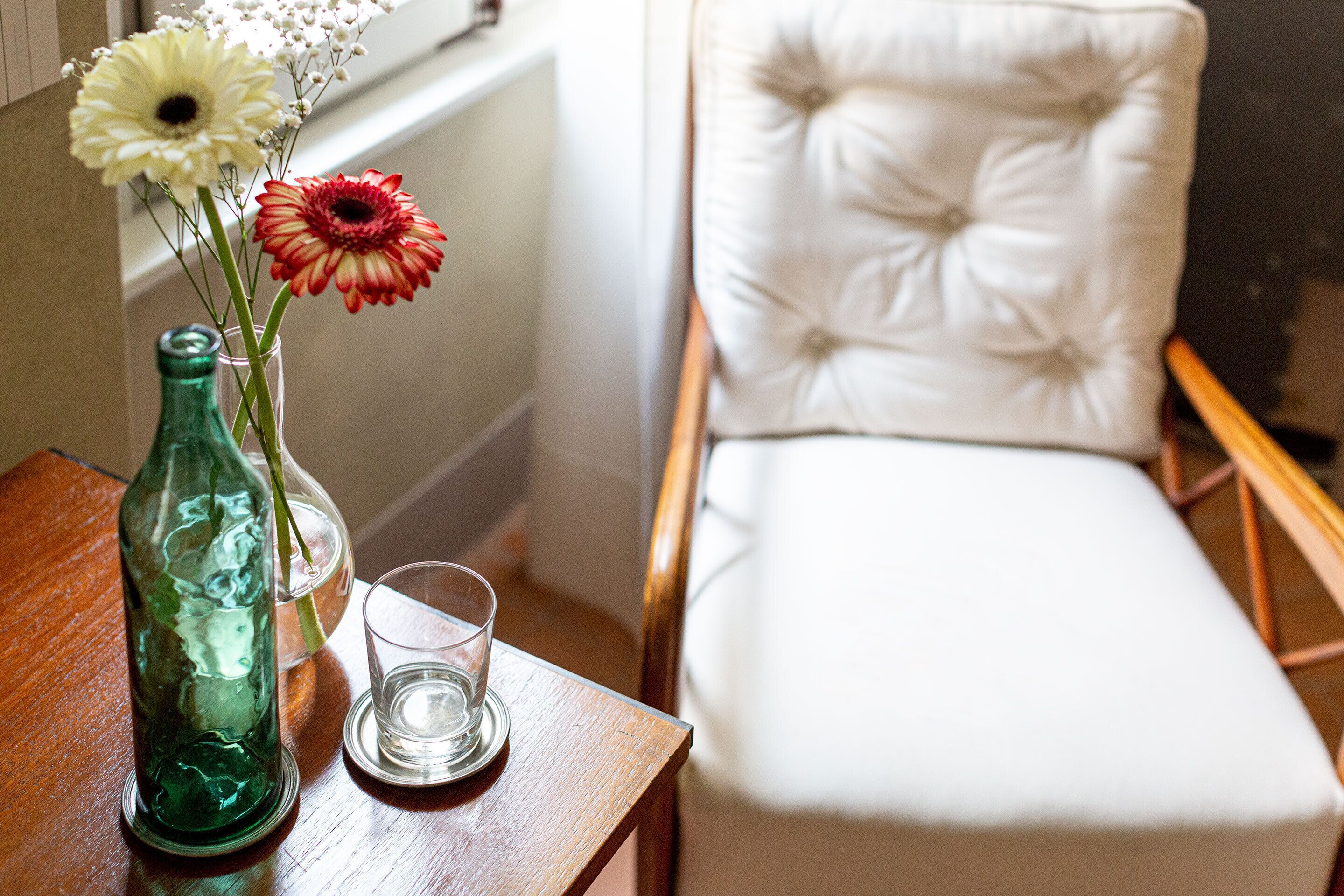 Una mesa de madera con una botella de vidrio verde, un vaso transparente y un florero con flores.