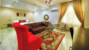 Una sala de estar con un sillón rojo, un sofá marrón, una mesita redonda y un tapete con estampado rojo y dorado.