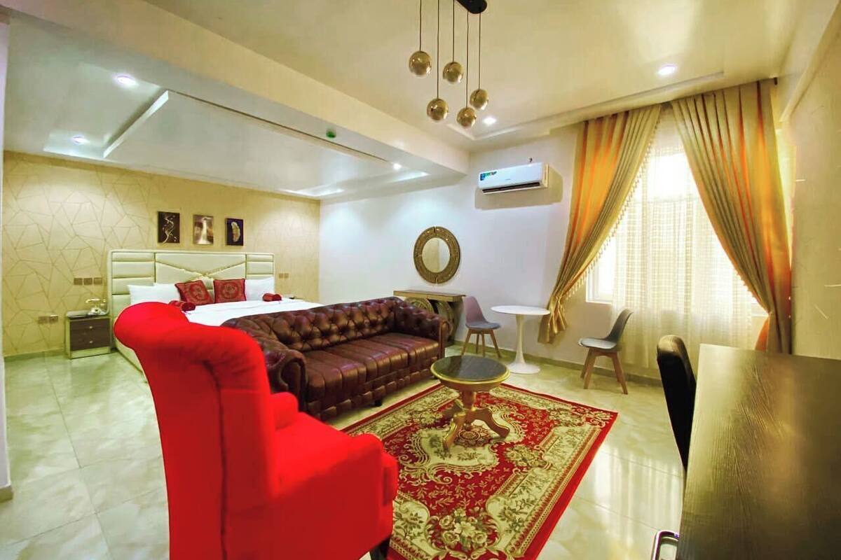A living room with a red armchair, a brown sofa, a small round table, and a red and gold patterned rug.