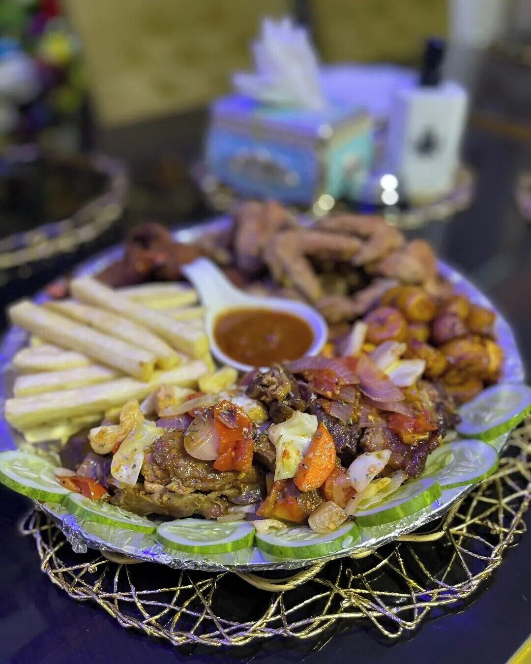 A plate of food with various items including meat, vegetables, and fries, accompanied by a small bowl of sauce.