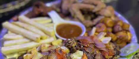 A plate of food with various items including meat, vegetables, and fries, accompanied by a small bowl of sauce.