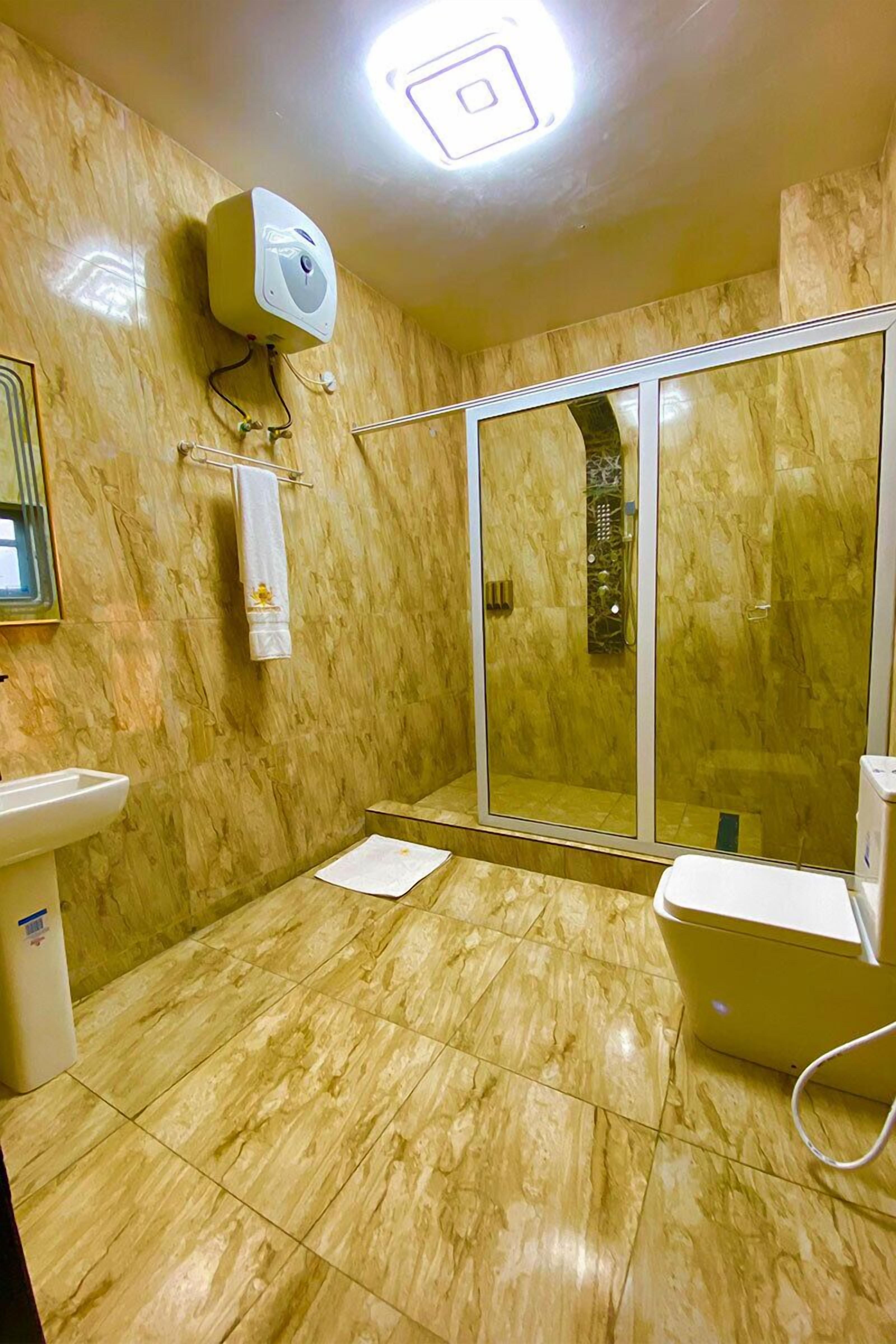 A bathroom with a marble floor, a glass shower enclosure, a toilet, a sink, and a towel rack.