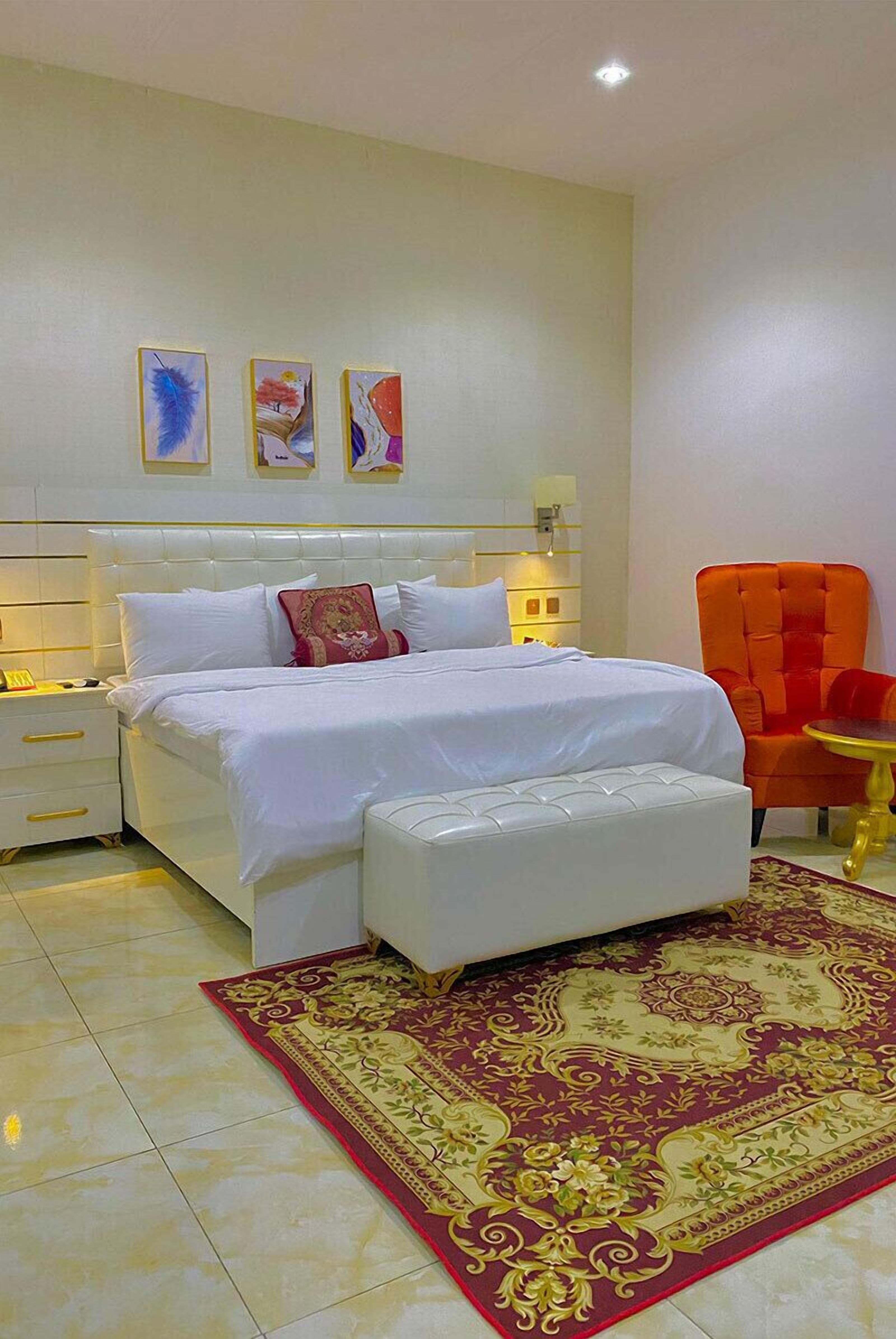 A bedroom with a large bed, a bedside table, a chair, and a decorative rug.