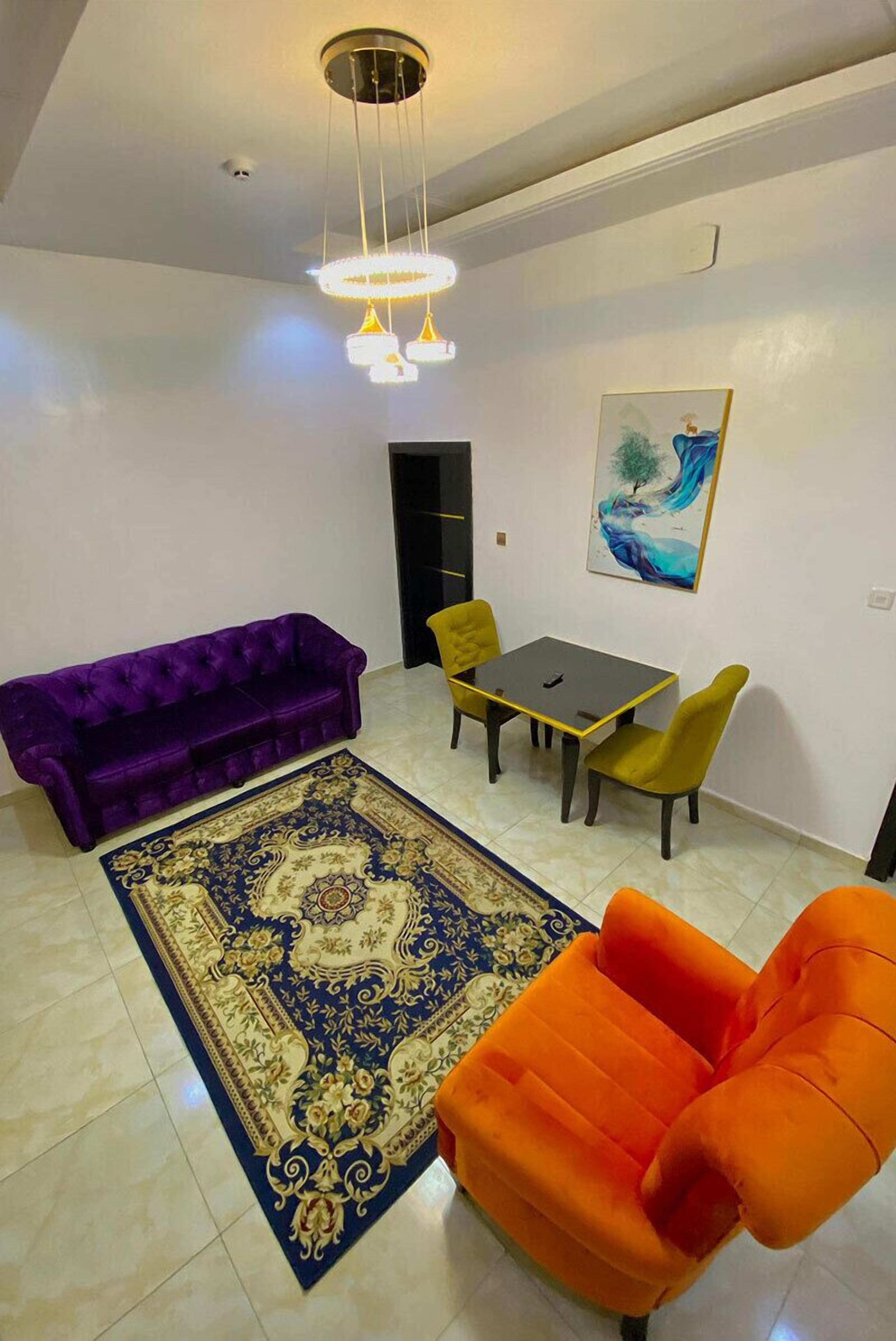 Una sala de estar con un sofá púrpura, una mesa amarilla y un sillón naranja.
