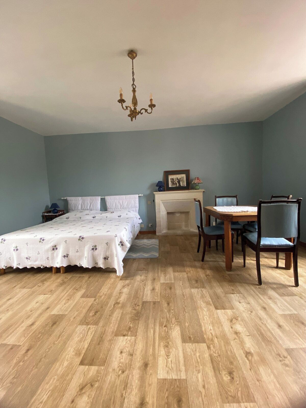 Une chambre à coucher avec un lit, une table à manger avec des chaises, une cheminée et un lustre.