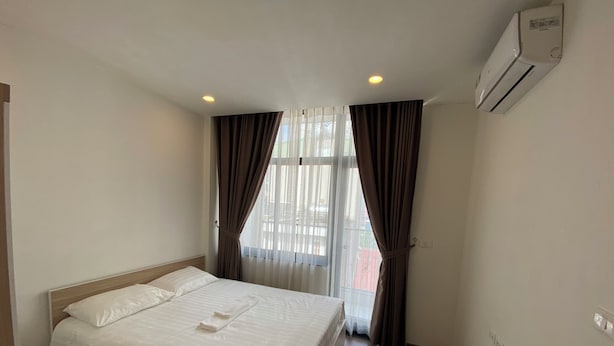 Een hotelkamer met een bed, gordijnen, een raam en een airconditioning.
