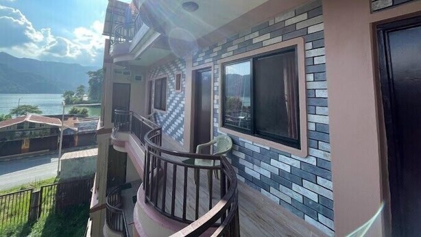 A residential building with a balcony, large windows, and a view of a body of water and mountains. - Yuriko Guest House (Pokhara)
