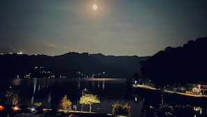 A nighttime view of a lake with a full moon, calm water, and surrounding hills. - Yuriko Guest House (Pokhara)