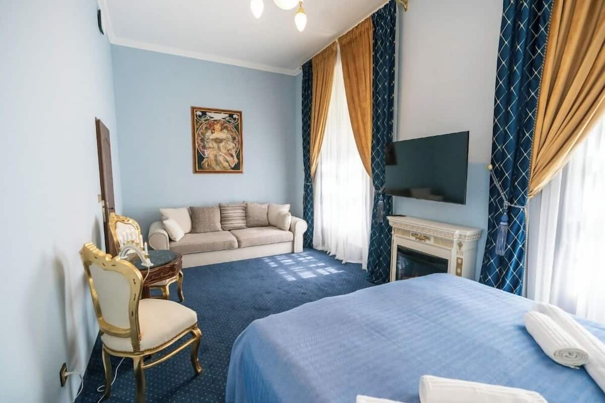 A hotel room with a bed, a sofa, a fireplace, and a television.