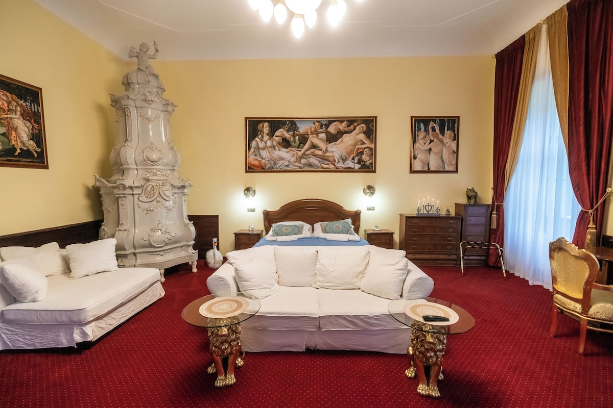 A hotel room with a large bed, a sofa, two side tables, a wooden cabinet, and artwork on the walls.