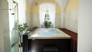Een badkamer met een jacuzzi, een douchecabine van glas en een plant in pot.