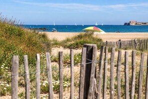 A beach with a wooden fence in the foreground, a sandy beach, and sailboats on the water.