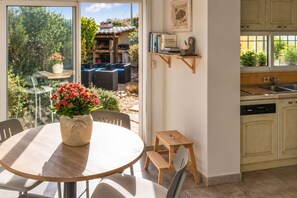 A kitchen with a dishwasher, a small wooden stool, and a dining area with a table and chairs.