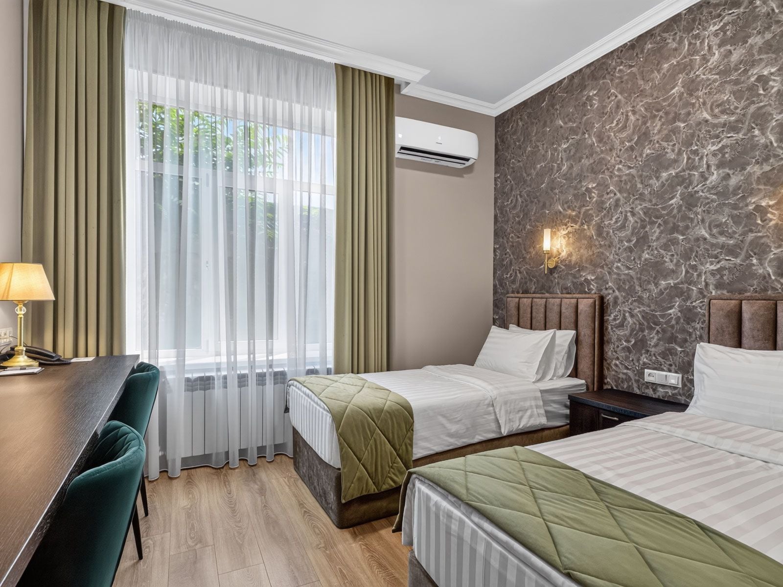 A hotel room with two beds, a desk, and a window with curtains.