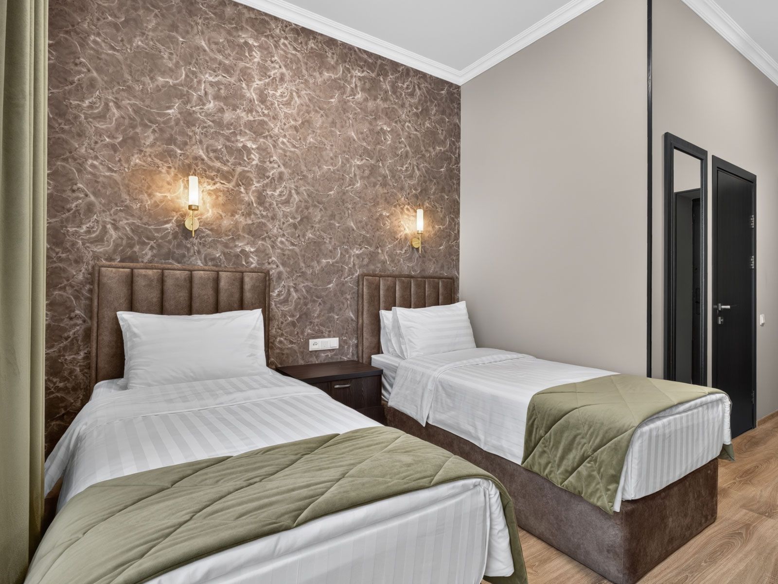 A hotel room with two beds, marble-patterned walls, and a door.
