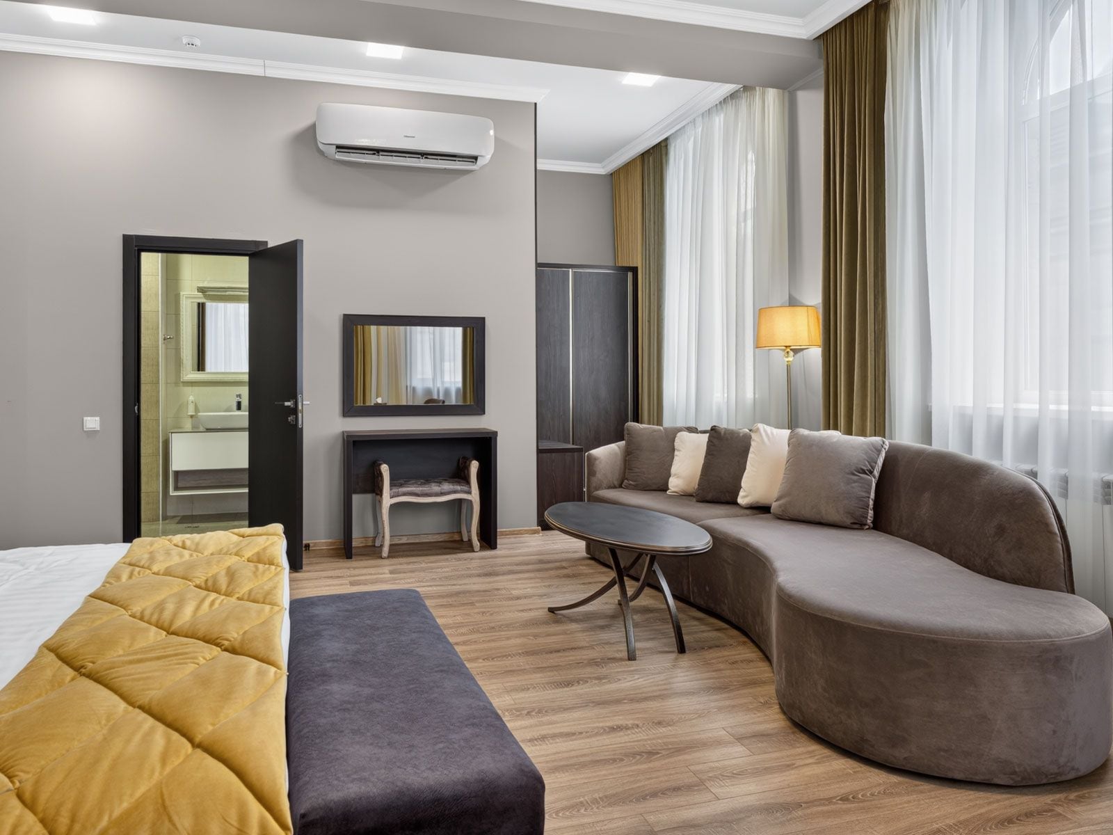 Habitación de hotel con cama, sofá, mesita, silla, aire acondicionado, espejo y lámpara.