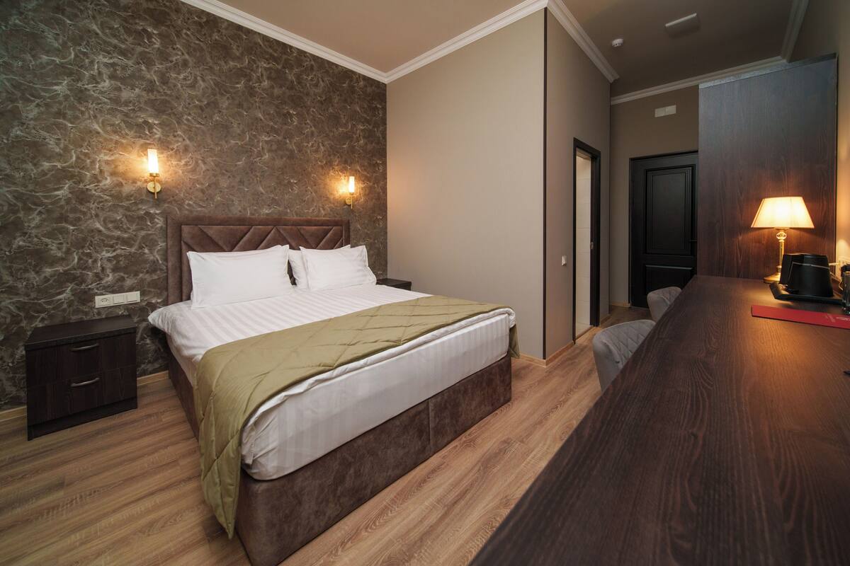 A bedroom with a bed, nightstands, a wooden dresser, a lamp, and a door.