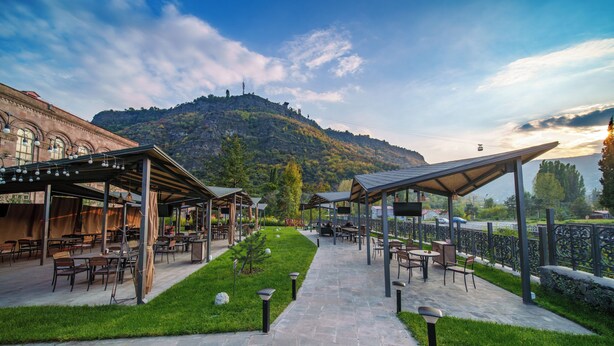 An outdoor patio area with tables and chairs, a stone pathway, and a view of a mountain.