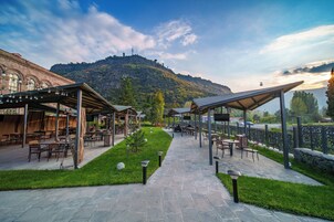 Un patio al aire libre con mesas y sillas, un camino de piedra y vistas a la montaña.