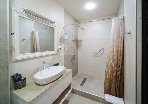 Une salle de bain moderne avec un lavabo blanc, un miroir, une douche avec une porte en verre et un sol carrelé de couleur beige.