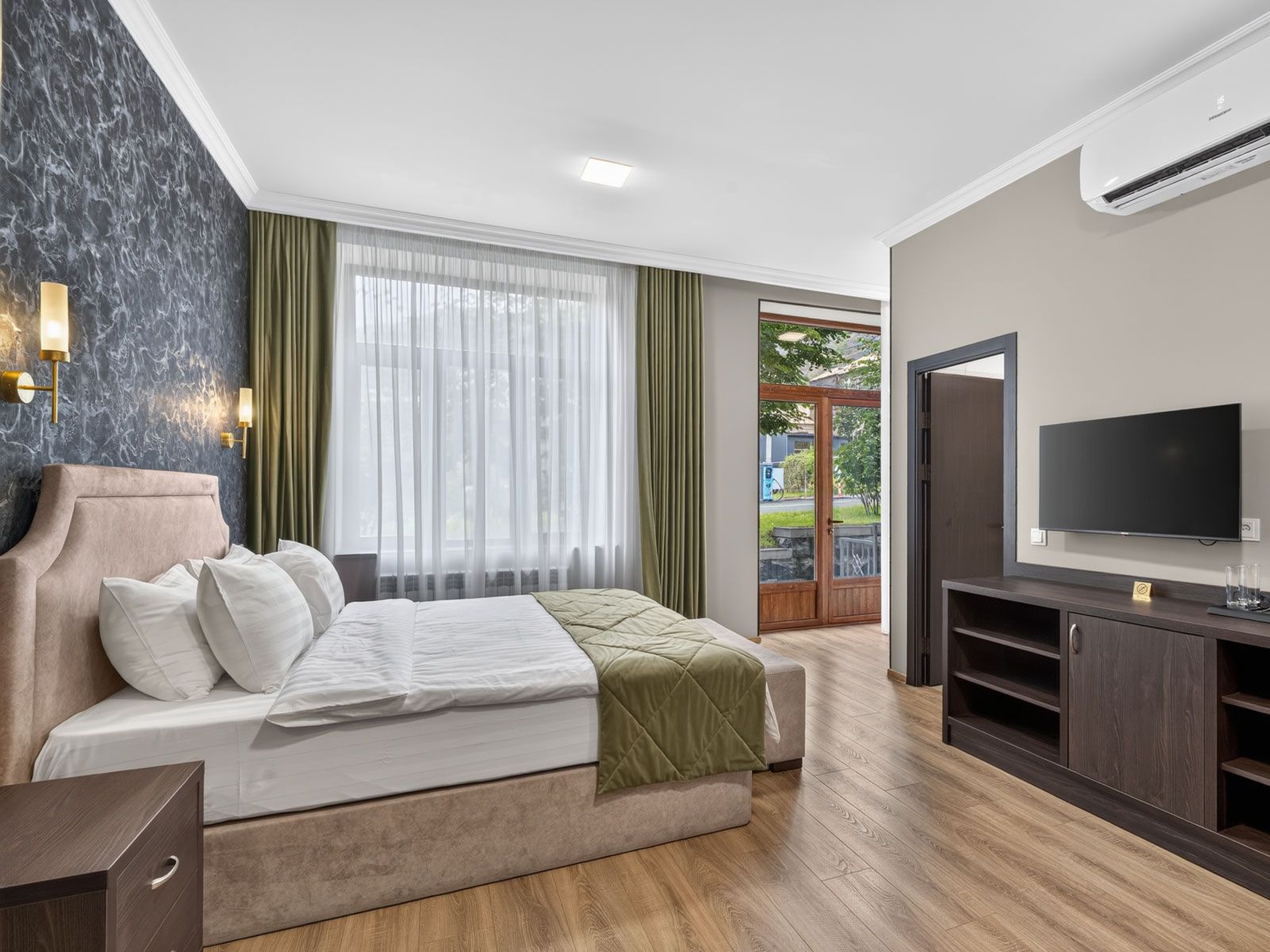 A hotel room with a bed, a television, a desk, and a view of the outdoors.