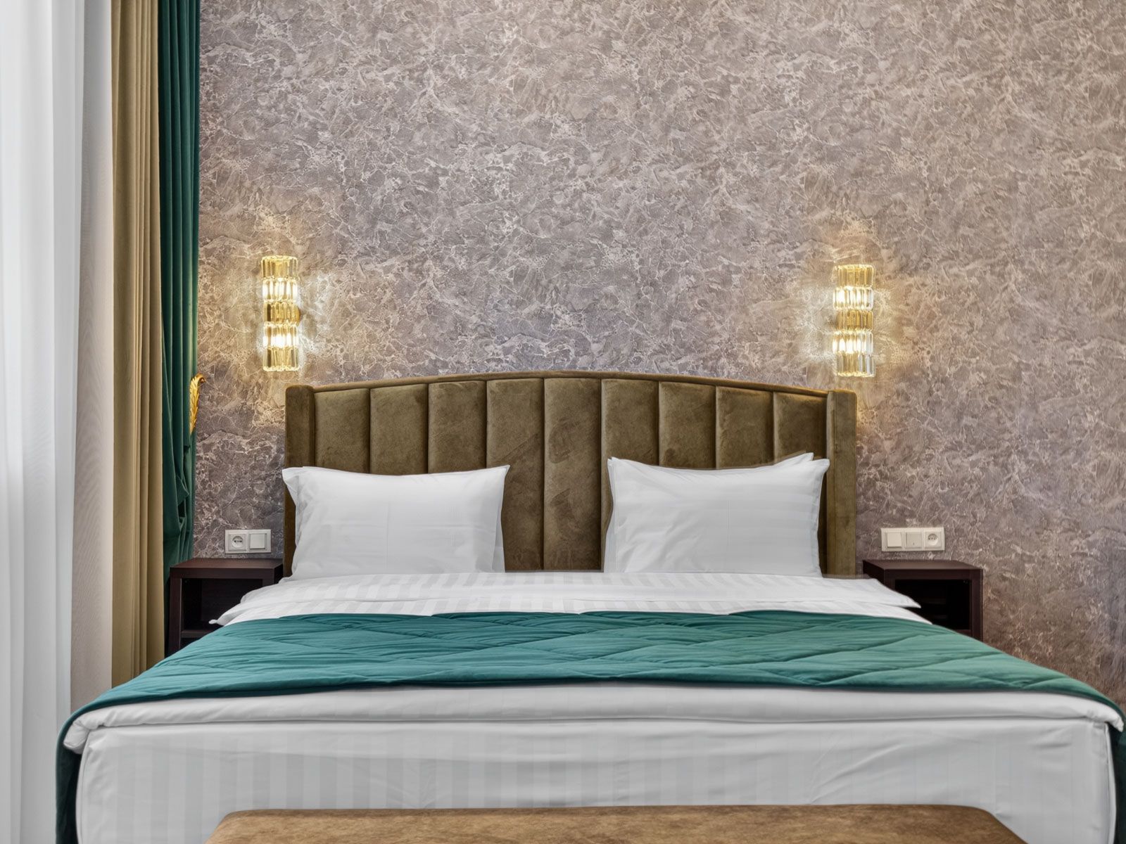 Una cama con cabecera, dos mesitas de noche y luces fijadas en la pared.