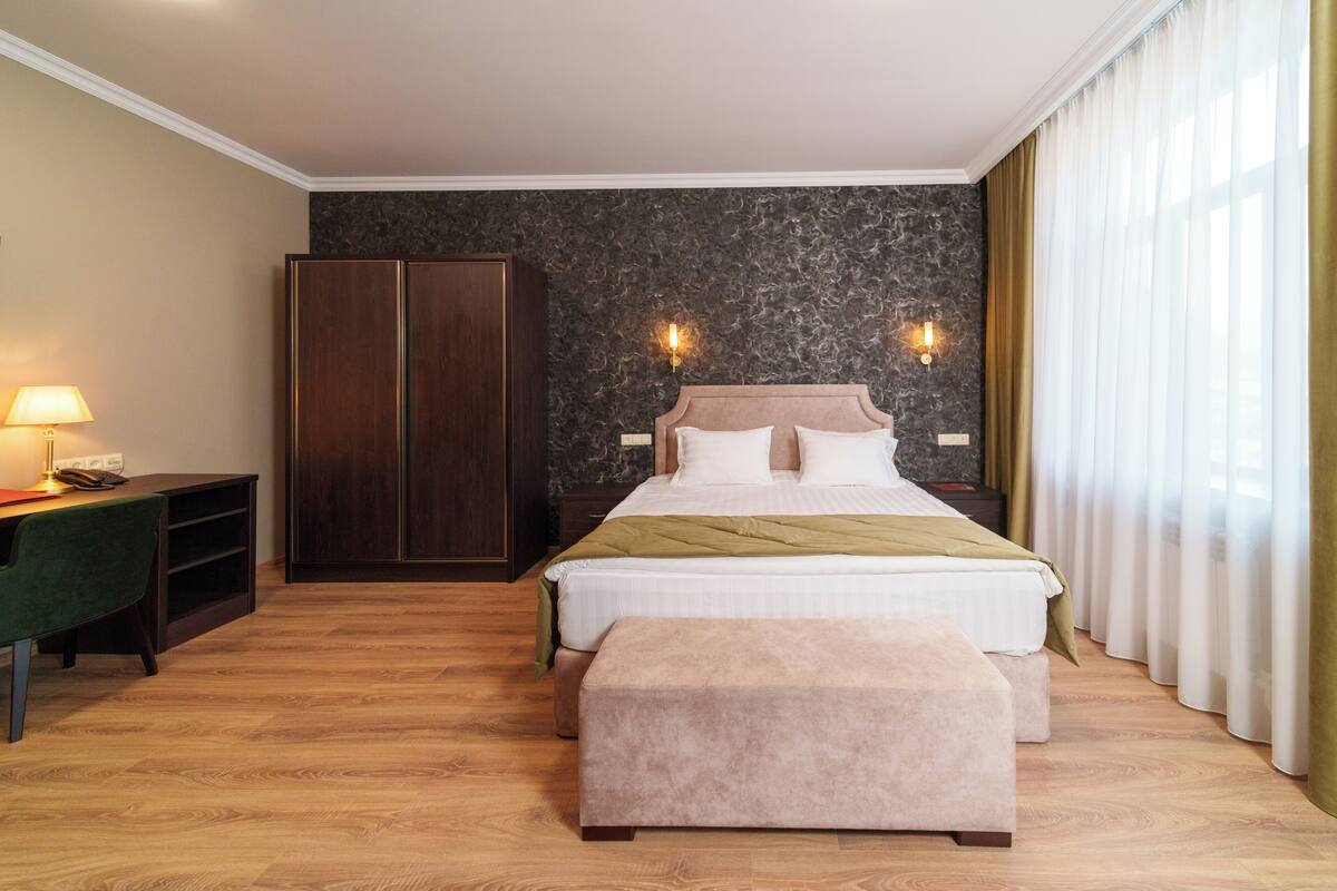 A hotel room with a bed, a desk, a wardrobe, and a window with curtains.