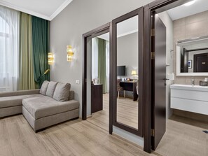 Une chambre d’hôtel moderne équipée d’un canapé, d’un bureau, d’un miroir et d’une salle de bain avec un lavabo et un miroir.