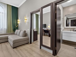 Una habitación de hotel moderna con sofá, escritorio, espejo y baño con lavamanos y espejo.