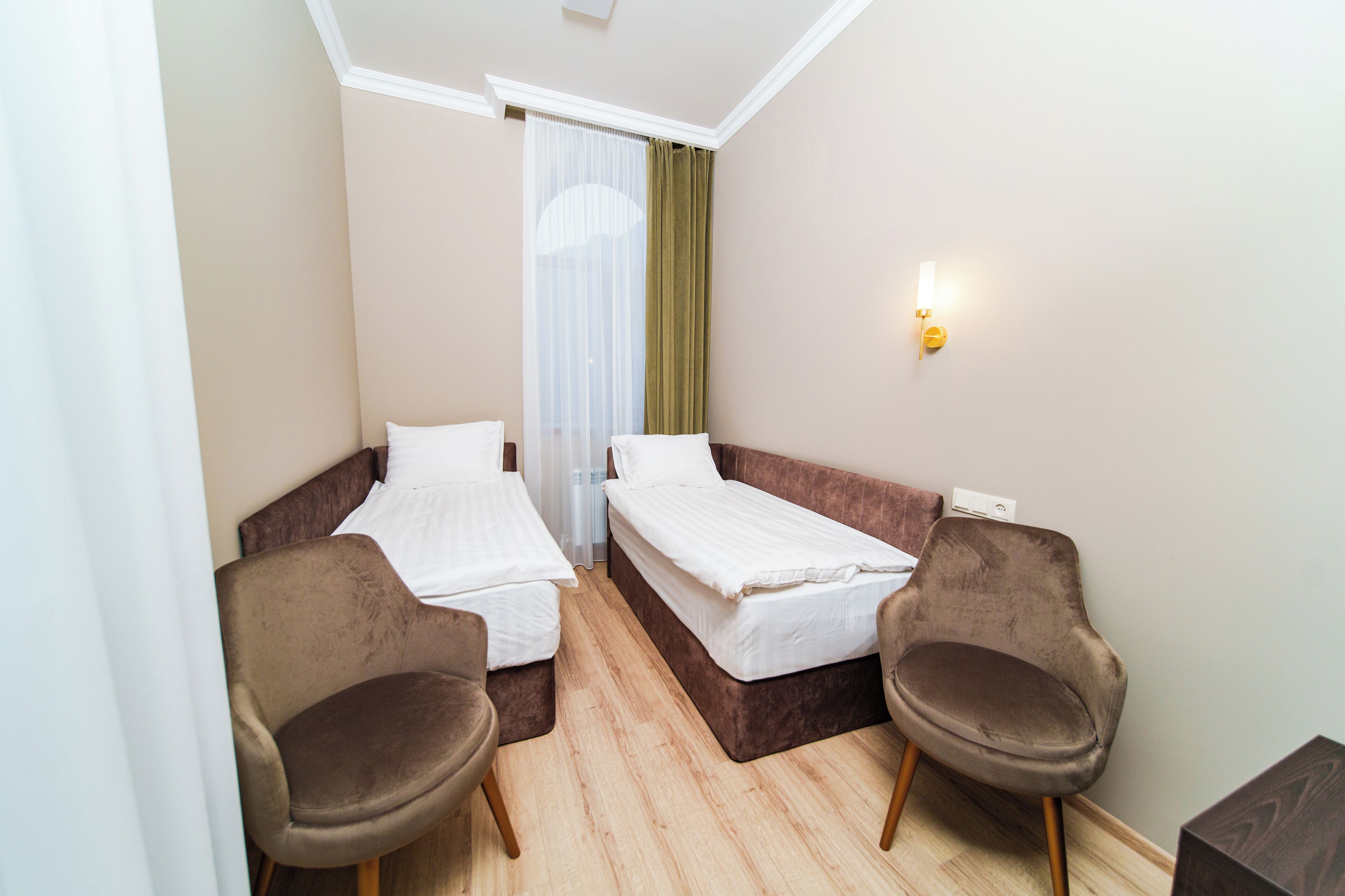 A small, well-lit room with two single beds, a pair of armchairs, and a wooden floor.