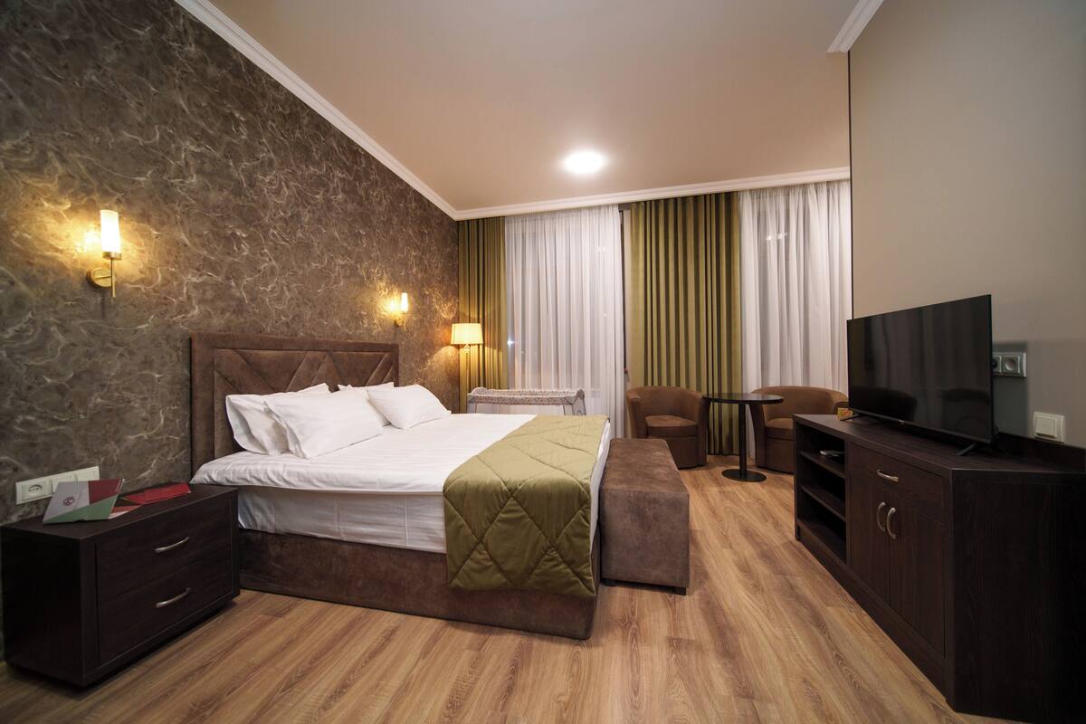 A modern hotel room with a bed, bedside tables, a TV, and a seating area.