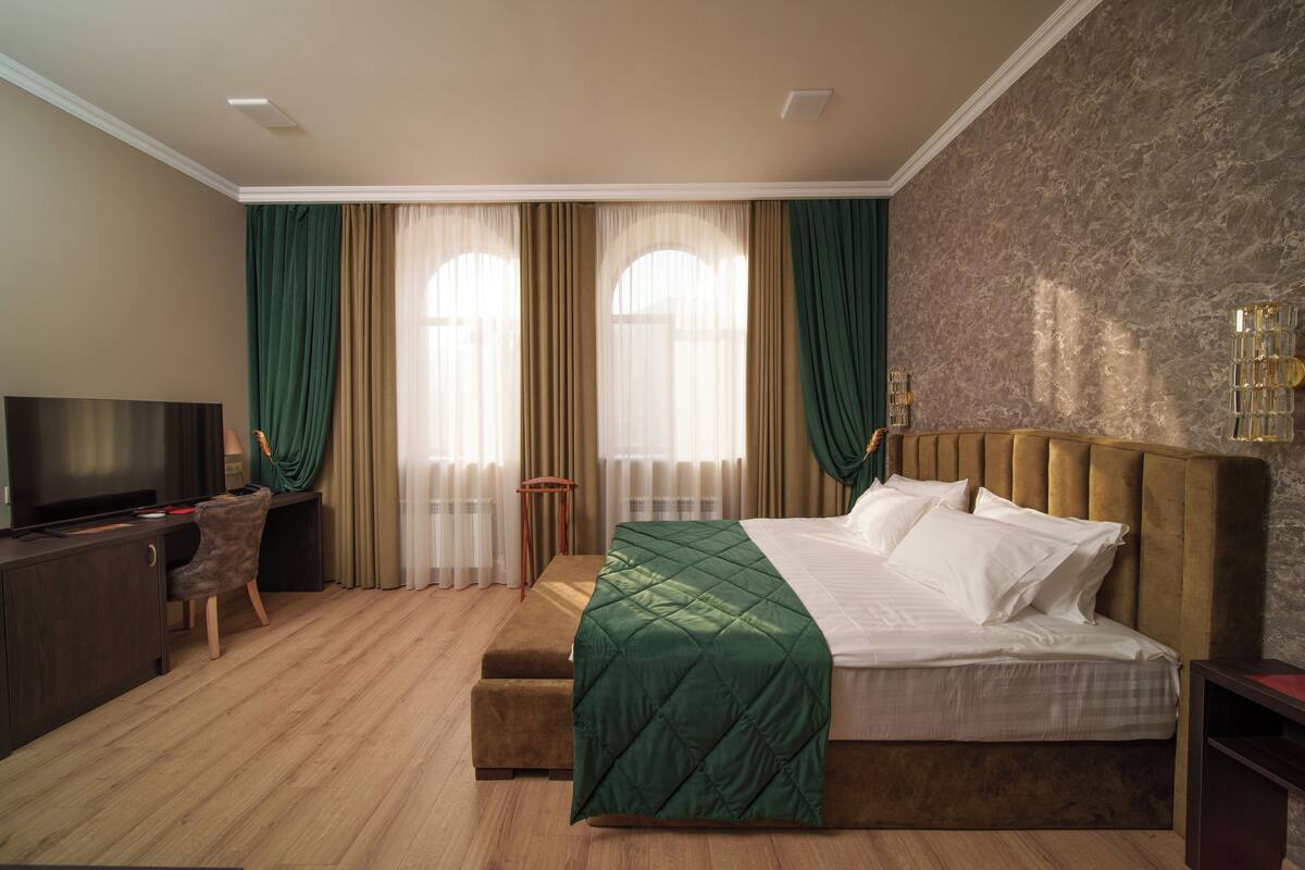 A hotel room with a large bed, a TV, a desk, and a chair.