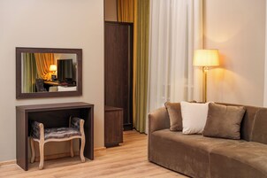 Una habitación de hotel moderna con una mesa consola de madera, un sillón acolchado, un sofá marrón con dos cojines, una lámpara de pie y un espejo grande que refleja la habitación.
