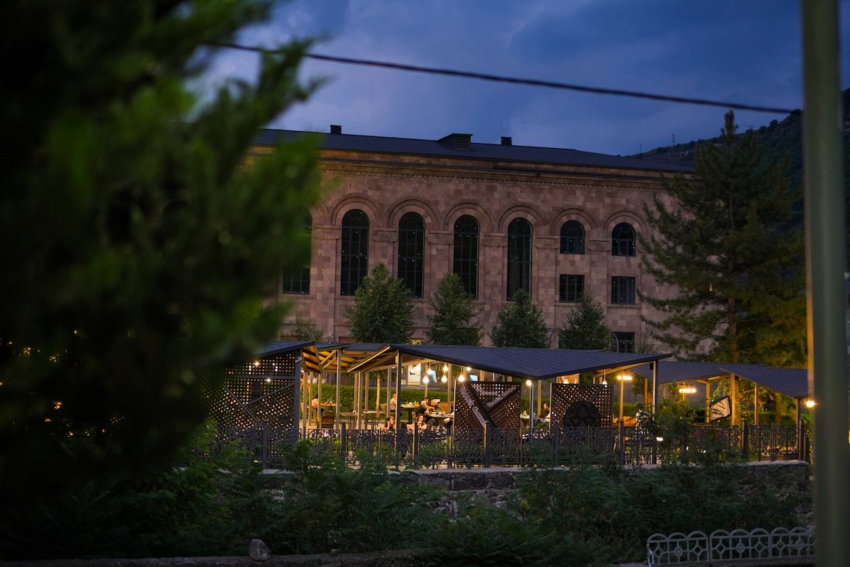 A building with arched windows and a covered outdoor seating area with tables and chairs.