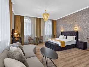 Una camera d'albergo con un letto grande, un divano, un piccolo tavolino rotondo e una scrivania con una lampada.