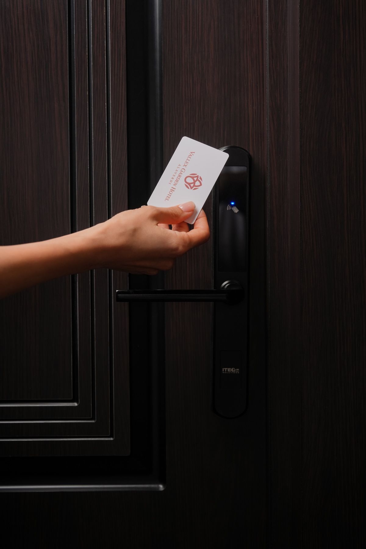 A hand holding a card near a modern door lock with a digital display.