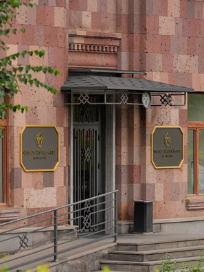 L’entrée d’un hôtel se distingue par sa façade à motifs en damier, une grille d’entrée et deux panneaux indiquant le nom de l’hôtel.