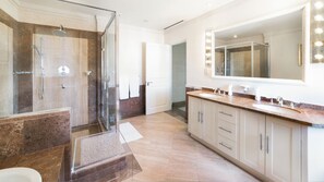 A modern bathroom with a glass-enclosed shower, a large mirror with lights, and a vanity with a sink and cabinets. - Smugglers Cove 6 (4 bed): Beachfront condo (Paynes Bay)
