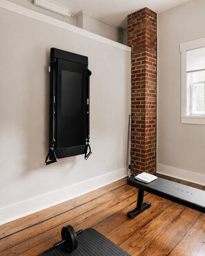 A room with a brick fireplace, a pull-up bar, and a bench. - Hot Tub, 2 Fire Pits, Pond, Tonal & Pet-Friendly (Eldred)