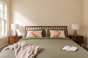 A neatly made bed with pillows, a blanket, and a book on a wooden nightstand.