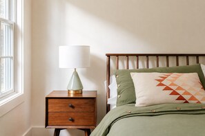 Una camera da letto con un comodino in legno, una lampada, un letto con biancheria verde e una finestra.