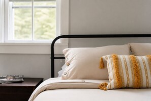 A bed with a black metal frame, beige bedding, and a patterned pillow. - Hot Tub, 2 Fire Pits, Pond, Tonal & Pet-Friendly (Eldred)
