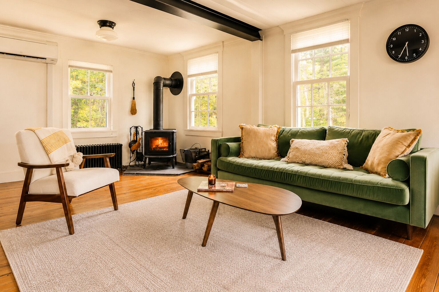 A living room with a green sofa, a wooden chair, a coffee table, a fireplace, and a clock on the wall.