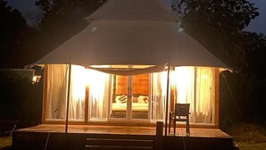 Un alloggio in tenda con un letto, tende e una sedia all'esterno.