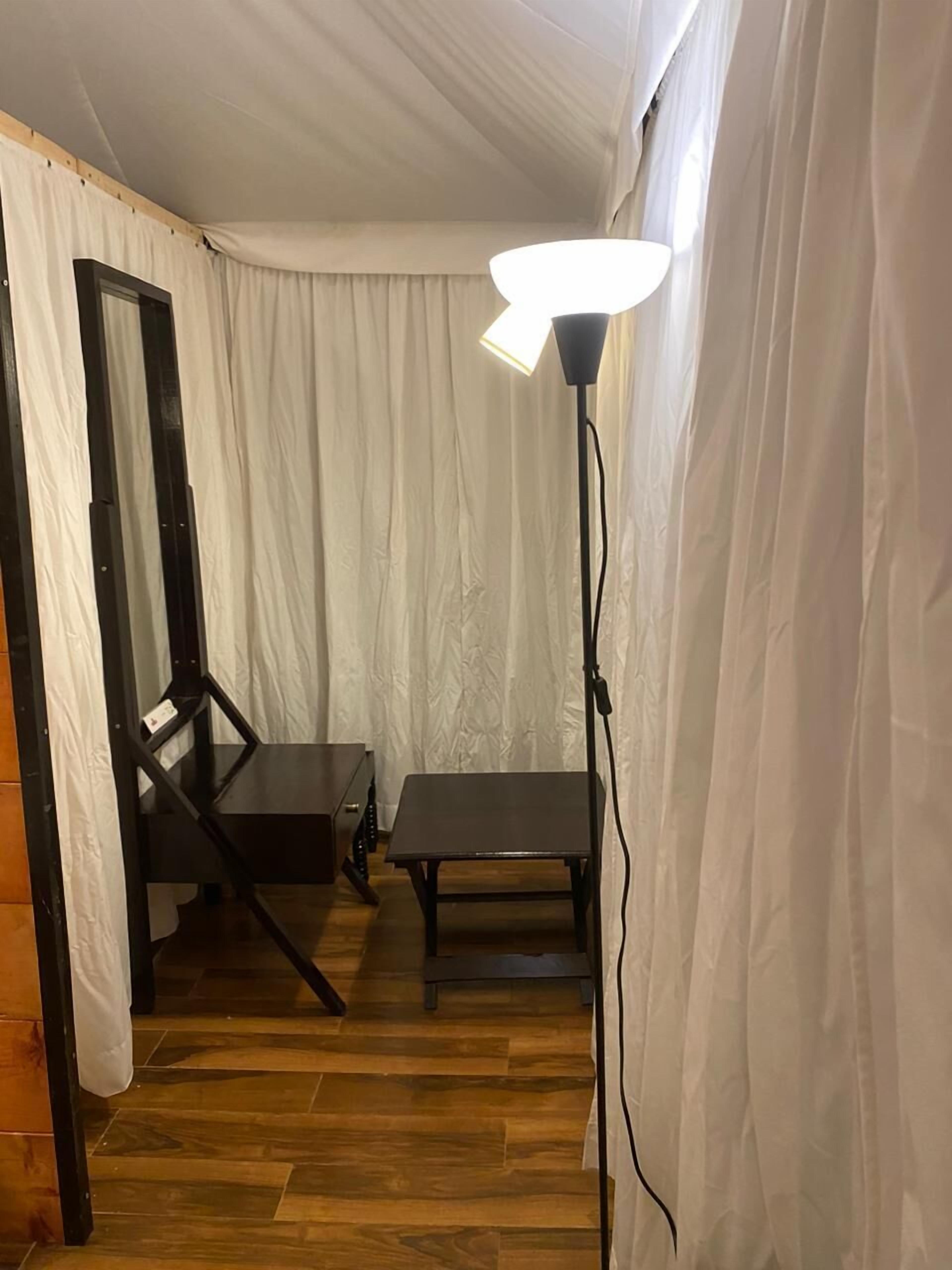 A room with a wooden floor, a table, a chair, and a floor lamp.
