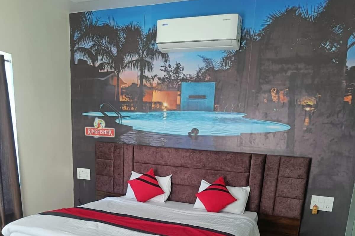 Una cama tamaño king con colcha y dos almohadas rojas y blancas, además de un plaid rojo. El cuarto tiene piso de madera y una alfombra estampada.