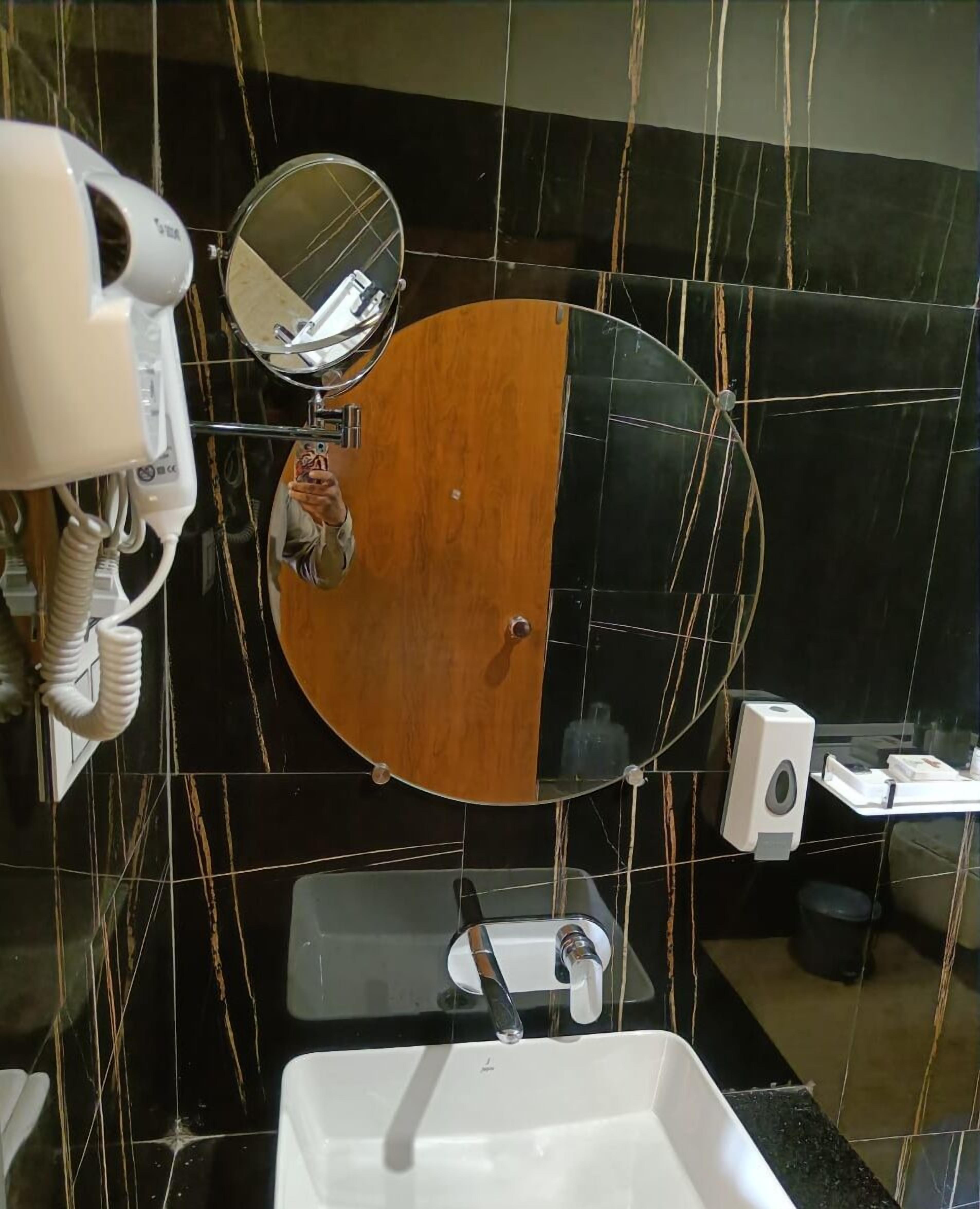 A bathroom with a wooden vanity, a mirror, a hairdryer, and a hand dryer.